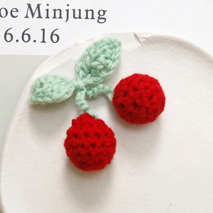 Macro view of handmade crochet cherry accessories with soft yarn texture on a ceramic plate