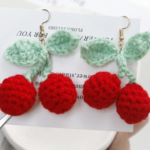 Close-up of handmade crochet cherry earrings with red yarn texture and gold hooks