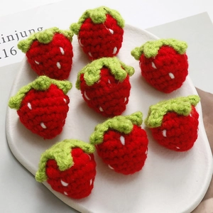 Detailed view of eight handmade crochet strawberry charms on a white ceramic tray