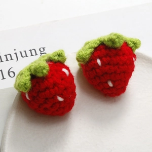 Detailed close-up of handmade crochet strawberry charms with red yarn and green leaves