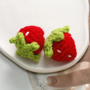 Macro detail of hand-knitted strawberry charms in red and green yarn on white ceramic