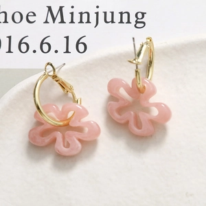 Détail de boucles d'oreilles fleur en résine rose avec anneaux dorés sur plateau