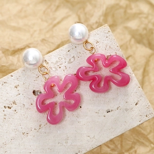 Détail de boucles d'oreilles fleurs en résine rose avec perles blanches et liens dorés