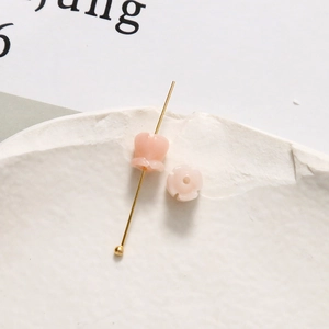 Makroaufnahme von zwei 6 mm rosa Maiglöckchen-Blütenperlen mit goldenem Stift auf Stein