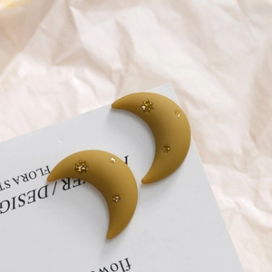 Close-up of ginger matte moon earrings with golden star details on a white display card