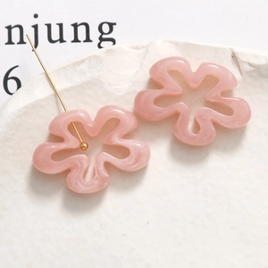 Détail de boucles d'oreilles fleurs en résine rose clair avec tiges dorées sur pierre