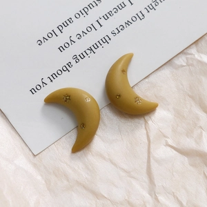 Detailed shot of crescent resin earrings in mustard yellow with gold star patterns