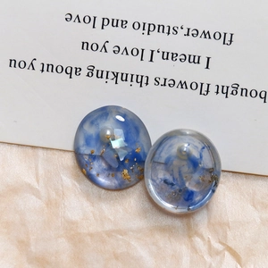 Detail van ronde hars oorbellen met blauwe rooktextuur, goudfolie vlokken en parelinleg