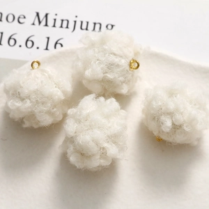 Close-up of four white plush lamb wool charms with small gold metal rings for DIY jewelry