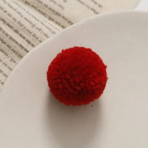 Detailopname van een rode handgemaakte wollen pompon op een vintage boekachtergrond