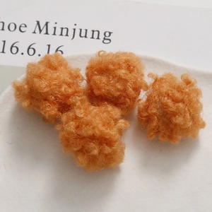 Close-up of four orange plush faux fur pom poms with curly texture for DIY crafts
