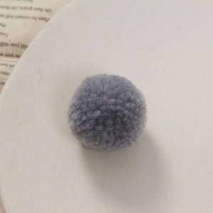 Close-up van een grijze gebreide pompon met zachte vezeltextuur voor DIY-handwerken