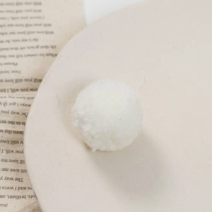 Macro-opname van een witte pluizige pompon voor DIY-ambacht op beige schotel