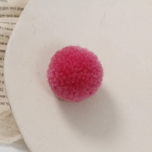 Detail van een pluizige roze pompon op een beige bord voor doe-het-zelf handwerkprojecten