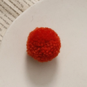 Detailopname van een handgemaakte oranje gebreide pompon voor DIY-accessoires en creatieve projecten