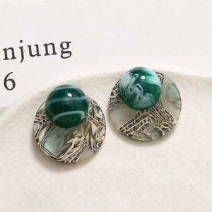 Close-up of retro acetate round earrings with green marble resin beads on ceramic tray
