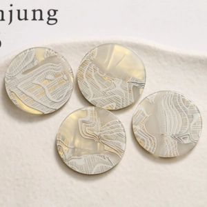 Macro view of four round beige acrylic charms with delicate white lace texture details