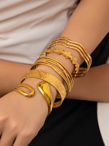 Dettaglio di bracciali a polsino dorati impilati con motivi a onde e finitura lucida