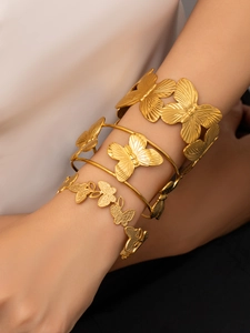 Dettaglio ravvicinato di un set di tre bracciali dorati con farfalle e texture a rilievo