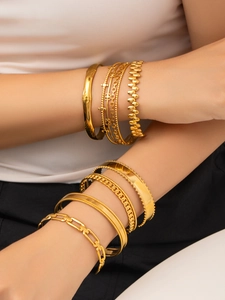 Dettaglio di bracciali sovrapposti placcati in oro con texture a bambù e a catena