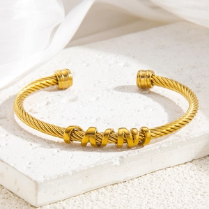 Gold twisted rope open bangle featuring five decorative rings on a stone display