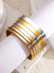 Close-up of five minimalist wide-surface open bangles in gold and silver polished finish