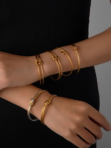 Primo piano di bracciali rigidi a nodo sovrapposti in oro e argento su un polso femminile