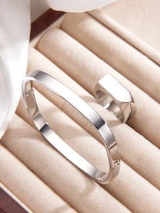 Detail of silver polished square bangle and signet ring set on cream velvet box