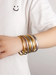 Set of six minimalist polished gold and silver steel bangles worn on a model's wrist