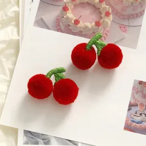 Flat lay of handmade red plush cherry accessories with green embroidery leaves on paper