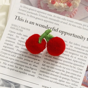 Macro shot of handmade crochet red cherry pompom accessory with green knitted leaves