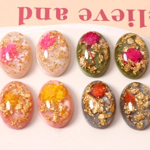 Makroaufnahme ovaler Harz-Cabochons mit echten Trockenblumen und Goldfolienflocken