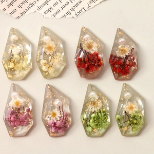 Detail view of multifaceted resin charms with dried flowers, gold foil and pearls