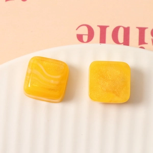 Macro detail of square yellow resin charms with smoky gold glitter and marble textures