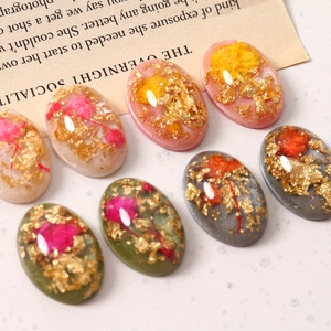 Makro-Detail von ovalen Harzanhängern mit Goldfolie und Trockenblumen für DIY-Schmuckherstellung