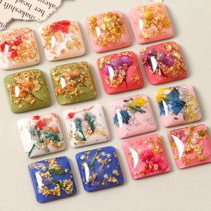 Macro view of square resin charms with dried flowers, gold foil, and pearls for DIY jewelry