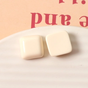 Close-up of cream square resin earrings with high-gloss finish on decorative ceramic plate