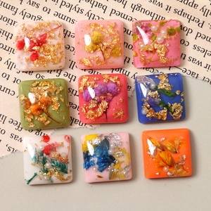 Detail of square resin charms with gold foil, dry flowers, and pearls for DIY jewelry