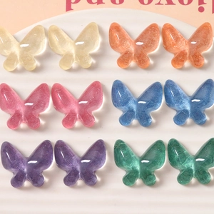 Macro detail of glitter resin butterfly charms in multiple colors on a textured tray