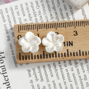 Macro detail of 11mm pearl white orchid nail charms on a wooden ruler for sizing