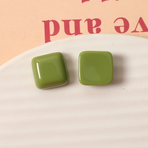 Macro detail of 15mm avocado green square resin studs on a white ceramic tray