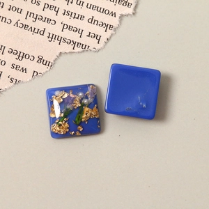 Close-up of square blue resin charms with embedded gold foil, pearls and dried flowers