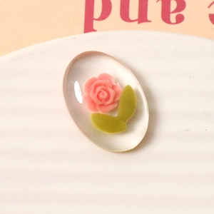 Macro shot of oval resin cabochon with pink rose and green leaf for DIY crafts