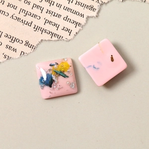 Detailed macro view of square resin charms with dried flowers, pearls, and gold foil accents