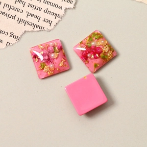 Detail of pink resin squares with embedded dried flowers, gold foil, and pearls for DIY crafts