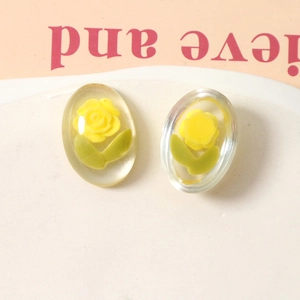 Close-up of oval transparent resin charms with 3D yellow roses and green leaves