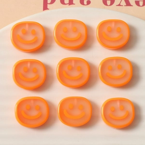 Macro shot of nine translucent orange resin smiley face charms on a white tray for DIY crafts