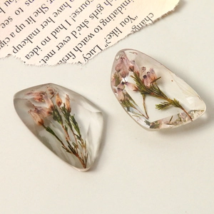 Detail of transparent resin charms with dried flowers on vintage paper background