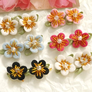 Detail of handcrafted woven floral hair clips with pearl centers and green ribbon leaves