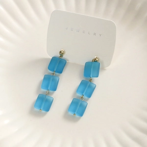 Dettaglio di perline di vetro quadrate blu opaco su eleganti orecchini pendenti oro